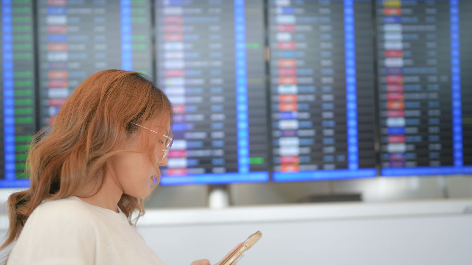 Woman with phone at airport departures board