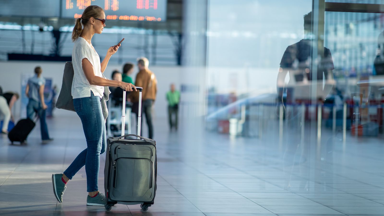 woman in an airport with phone and luggage